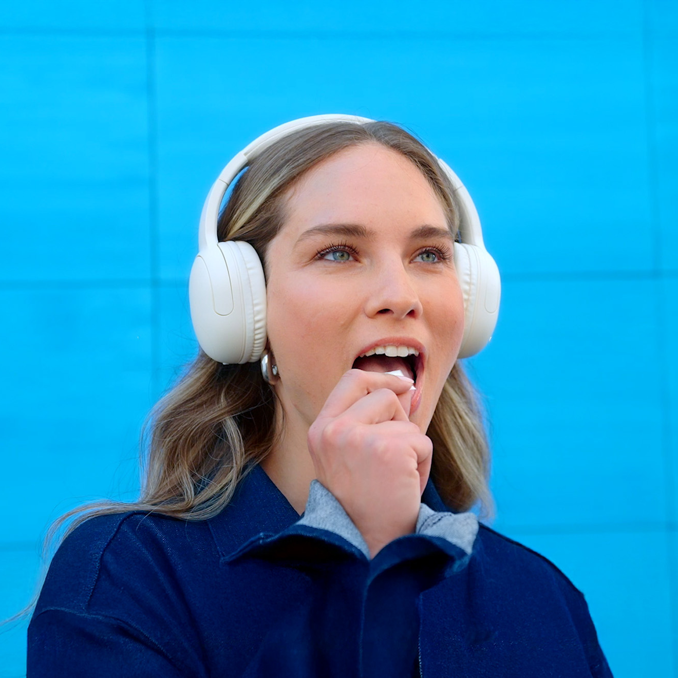 Woman with headphones, trying a ZYN nicotine pouch, in blue background